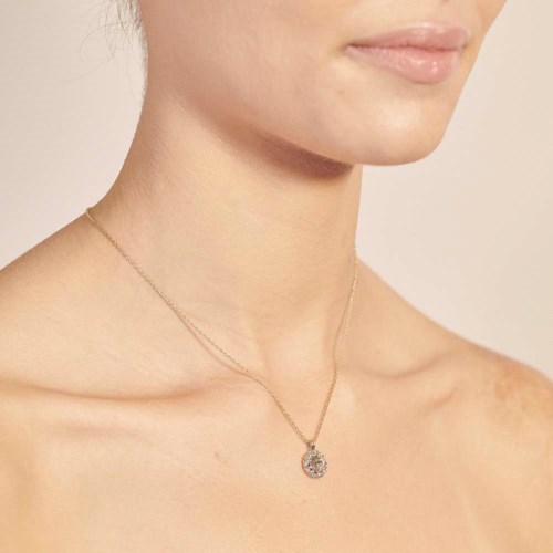 En kvinna har ett fint halsband med en cirkulär hänge, som visar hennes halslinje och en liten del av hennes läppar.