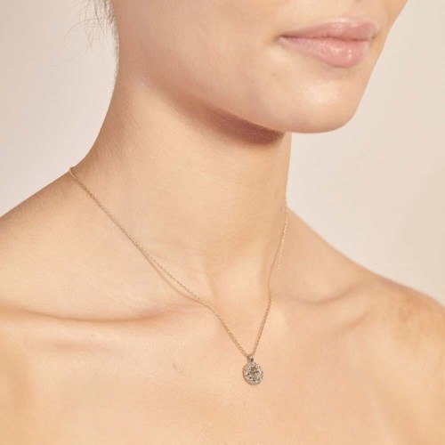 A necklace with a round pendant is on a woman’s neck, close to her collarbone, against her bare skin.