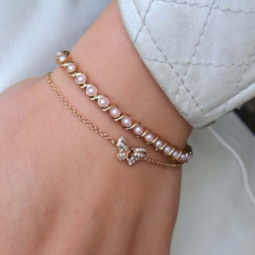 A close-up of a wrist with two gold and pearl bracelets, one featuring a butterfly charm.
