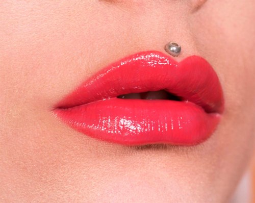 Närmre bild av läppar med glansigt rött läppstift och en näspiercing.