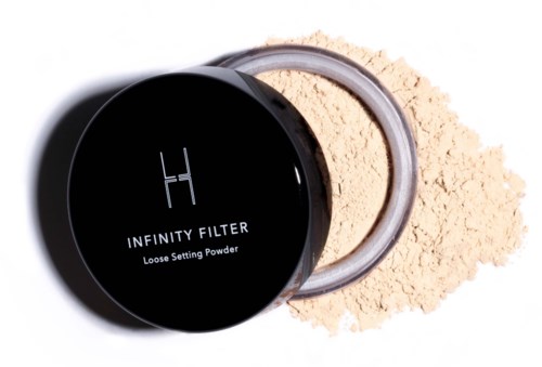 En svart rund beholder med merket "INFINITY FILTER" med løs pudder inni og spredd pudder rundt.