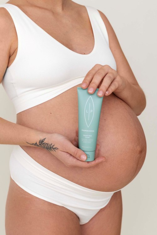 Pregnant woman holding a green skincare tube on her belly.
