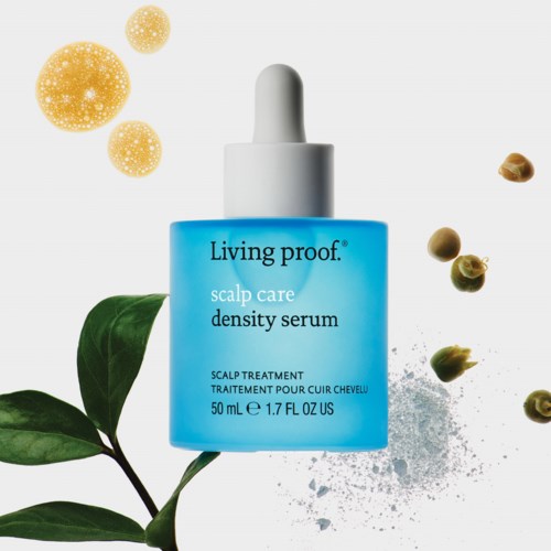 Blue serum bottle with dropper, surrounded by green leaves and small round particles, on a light background.