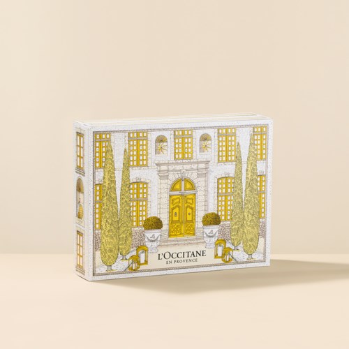 Decoratieve doos met een gedetailleerde illustratie van een landhuis met hoge bomen, gele ramen en een gouden deur.