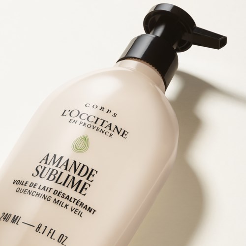Eine weiße Flasche mit Mandelduft-Bodylotion mit schwarzem Pumpspender, liegt auf einer beigefarbenen Oberfläche im Sonnenlicht.