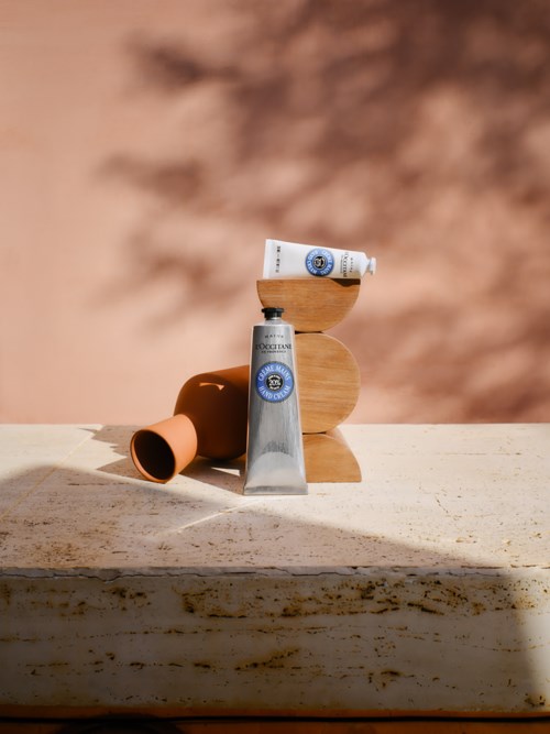 Eine Tube Creme, ein kleiner Behälter und ein Holzblock sind auf einer hellen Oberfläche mit schattigem Hintergrund arrangiert.