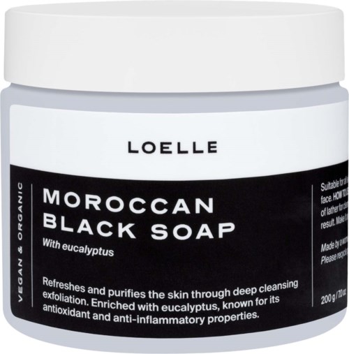 A white jar with a black label for Moroccan Black Soap with eucalyptus. The label explains its benefits for skin cleansing.