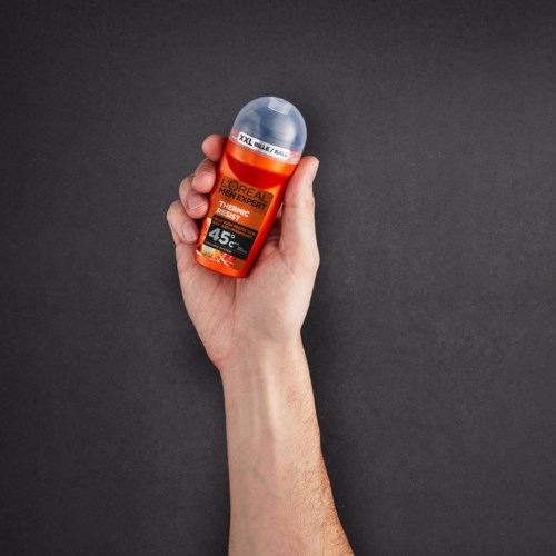 A hand holds a small orange bottle with a clear cap, labeled L'Oréal sunscreen, against a dark background.