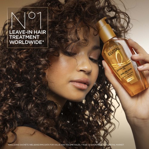 Woman with curly hair holding a gold bottle of hair treatment. The bottle has a label with gold and black colors.