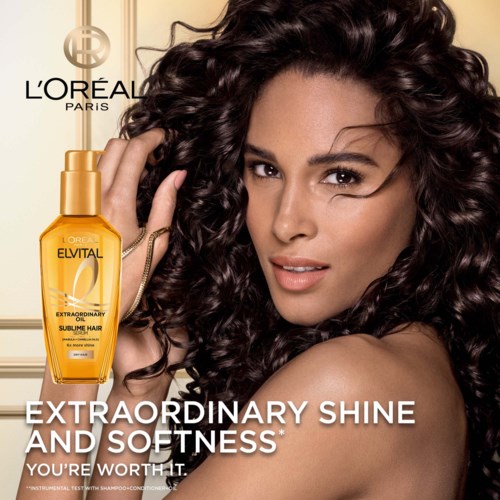 L'Oréal advertisement with a woman showing shiny, curly hair and a bottle of Elvital hair product.