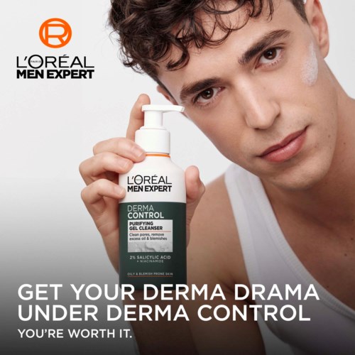 Junger Mann mit lockigem Haar, der eine Flasche Hautpflegeprodukt hält, bewirbt ein Gel-Reiniger für akneanfällige Haut.
