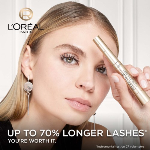 Een vrouw met lange wimpers gebruikt een gouden L'Oreal wenkbrauwserum en kijkt zelfverzekerd.