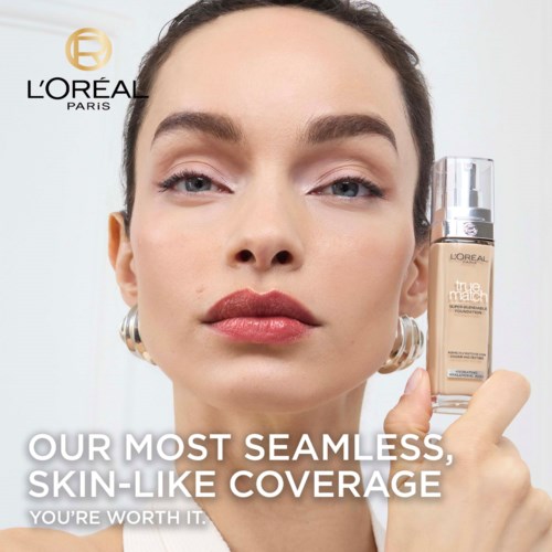 Eine Frau mit Make-up hält eine Foundation-Flasche, mit L'Oréal-Logo und Text über Hautabdeckung auf dem Bild.