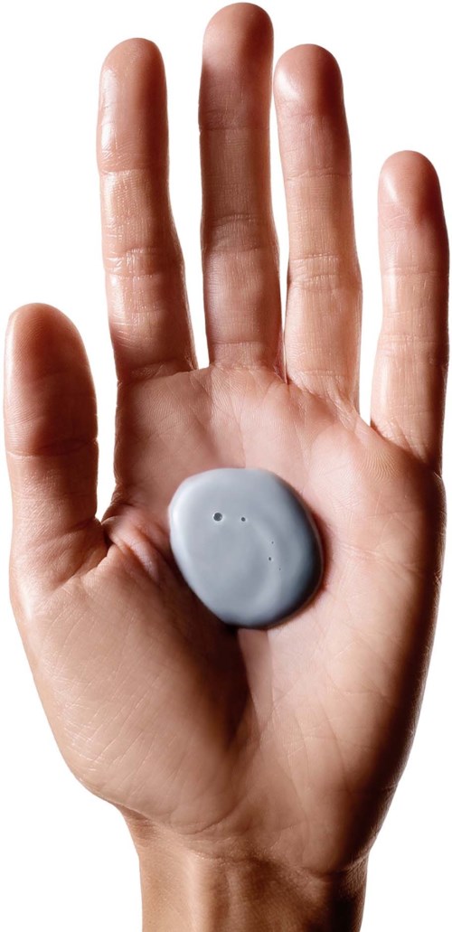 Eine Hand mit einem grauen runden Gegenstand in der Handfläche, Finger nach oben, vor hellem Hintergrund.