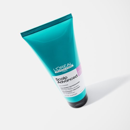 En blå tube med L'Oréal hodebunnsbehandling med hvite, svarte og lilla etiketter står på en hvit overflate.