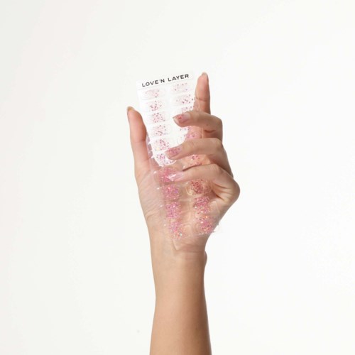 A hand holds a transparent sheet with pink glitter and text that says 'LOVEN LAYER'.