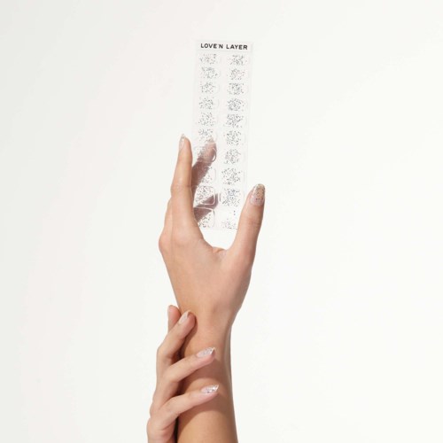 A hand holds a small transparent sheet with tiny, detailed designs and the text 'LOVE N LAYER' at the top.