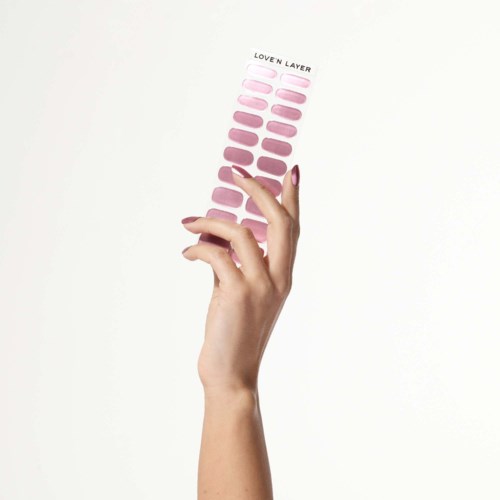 A hand holds a pink nail polish color palette with various shades from light to dark.