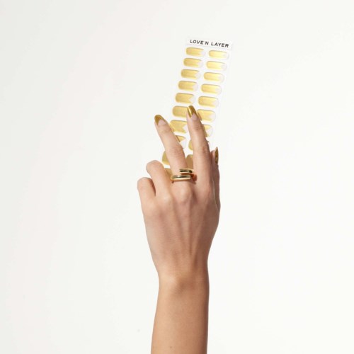 A hand with gold rings shows a sticker sheet labeled "Loving Layer" with yellow nail polish. The background is plain.