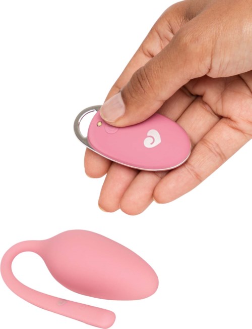 Eine Hand hält eine pinke Fernbedienung, verbunden mit einem pinken, eiförmigen Gerät mit einem Schlaufe. Das Gerät ist klein und glatt.