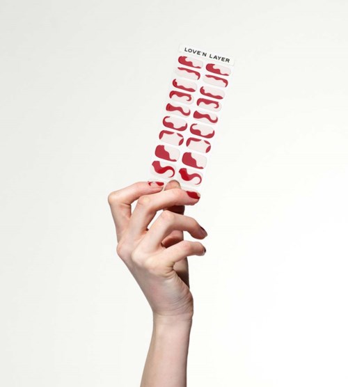 A hand holds a skincare product with a white and red label saying 'Love'n Layer' and 'Sun Protection 50+'.