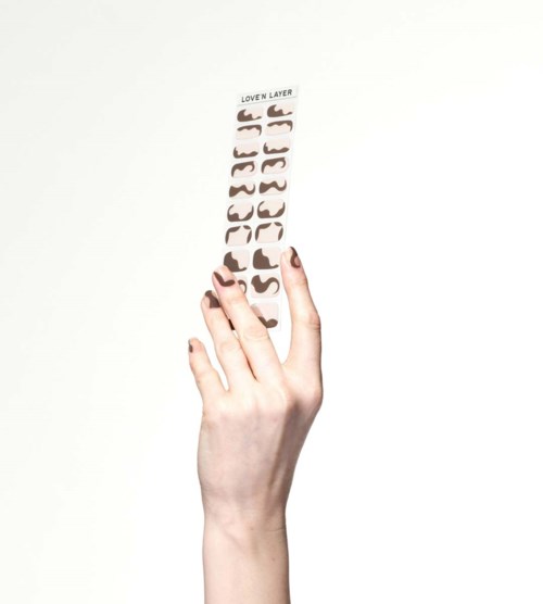 A hand holds a strip labeled "Lover Layer" with various lipstick shades on it, showing different colors.