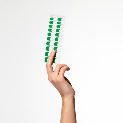 En hand håller ett blad med 14 gröna och vita medicinblåsor. Förpackningen innehåller mest används piller.