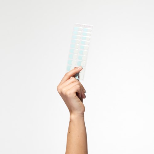 En hand håller ett blisterpaket med runda piller mot en enkel bakgrund.