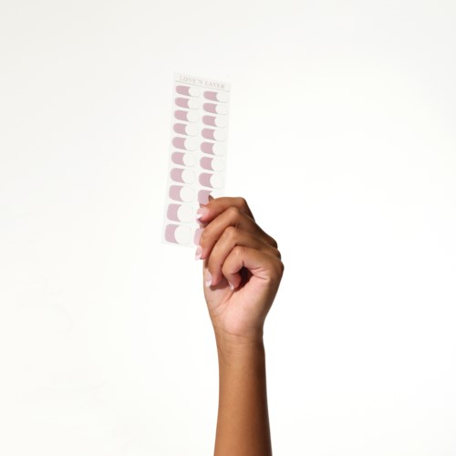 En hand håller ett rosa klistermärkesark med cirklar och text längst upp, mot en enkel vit bakgrund.