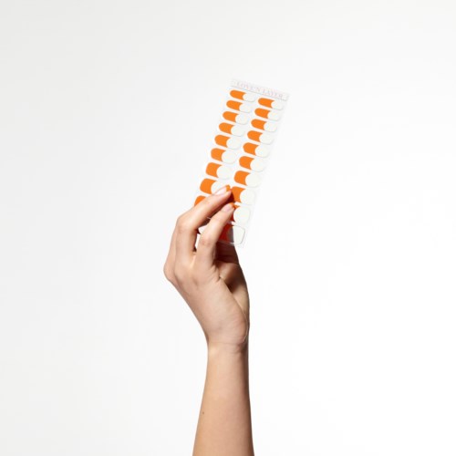 En hand håller en remsa med orange och vita tabletter mot en vit bakgrund.