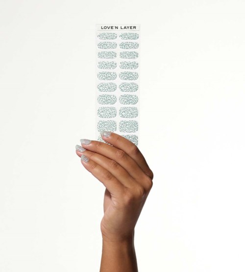 A hand holds a strip of decorative nail stickers called Love'n Layer with blue patterns on a white background.