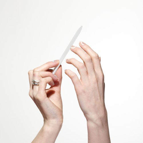 En persons händer håller en nagelfil mot naglar, med en ljus bakgrund.