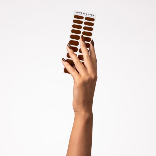 A hand holds a strip of brown adhesive patches labeled "LOVEN LAYER" against a plain white background.
