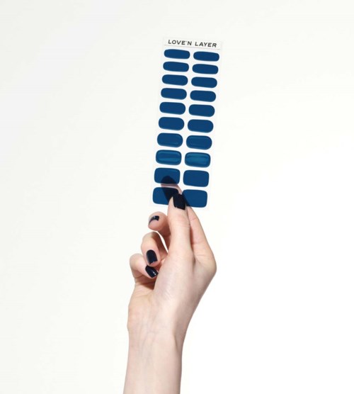 A hand holding a stick-on eyebrow product labeled 'Love Layer' with blue adhesive strips. The background is white.