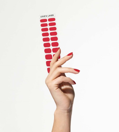 A hand with red nail polish holds a strip with red ovals and the text "LOVEN LAYER".