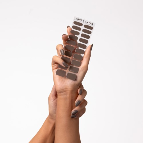 A hand holds a sticker sheet with various shades of brown nail polish samples, labeled "Love N Layer."