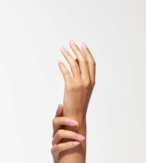 A person holds their hand up with fingers extended, nails painted pink, against a white background.