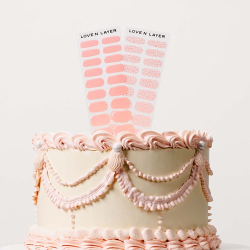 A decorated cake with pink and white icing, pearls, and draped garlands. Two sticker sheets are placed behind the cake.