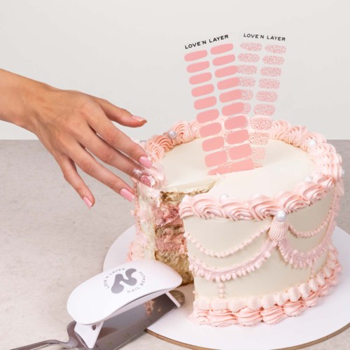 A decorated cake with pink and white icing, being cut with a knife, and a hand holding the knife.