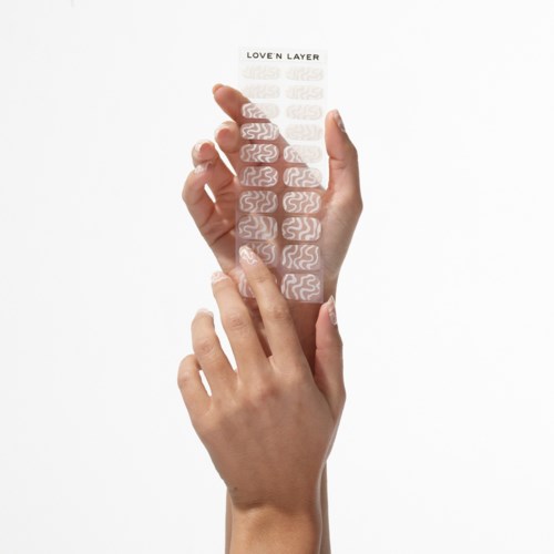 A hand peels a strip with layered text titled 'LOVE'N LAYER'. The strip has repeating wave patterns. White background.