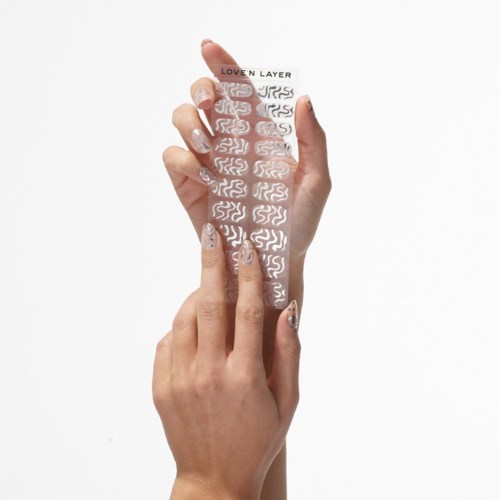 A person applies a transparent nail sticker with white swirl patterns to fingernails.