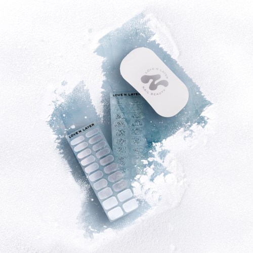 A skincare product set including a white container, a strip of patches, and a small booklet, all on a snowy surface.