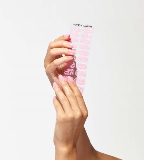 A hand holds a pink sheet with multiple pink and glittery nail stickers, labeled 'LOVE'N LAYER'.