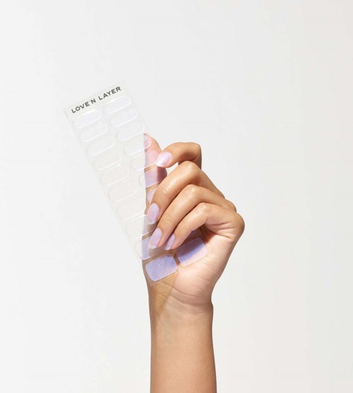 A hand holds a transparent nail sticker sheet labeled 'LOVEN LAYER' with multiple strips.