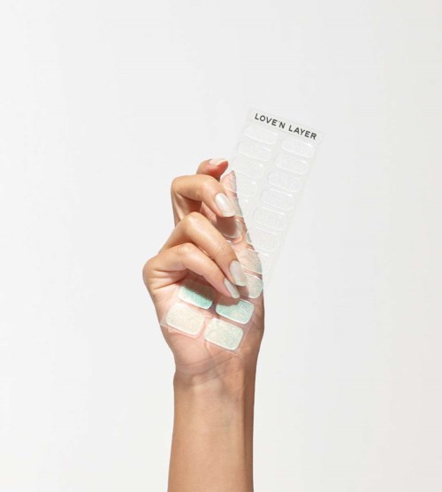A hand holds a sheet labeled 'LOVEN LAYER' with small nail polish sheets, against a plain background.