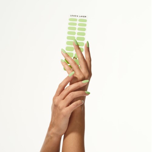 Two hands with green nail polish hold a sticker sheet titled "Love N Layer" with green ovals.