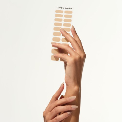 En hand håller en remsa märkt "Love N Layer" med beige nyanser, troligen foundation eller concealer.