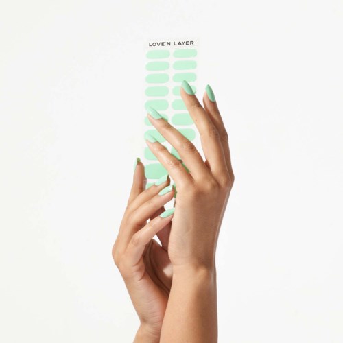 A hand with pastel green nails holds a sheet with a list titled "LOVE N LAYER," with several light green stickers.