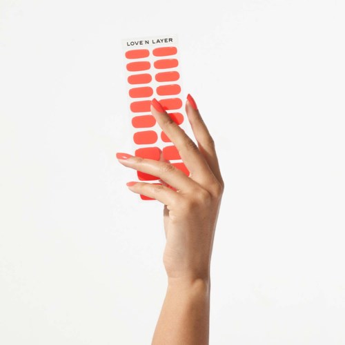 En hand håller en remsa med röd nagellackfärg klickar märkt "Lover Layer."