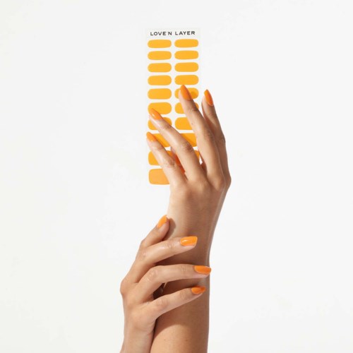 A hand with orange nail polish holds a yellow sticker sheet with the words 'Love'n Layer' at the top.